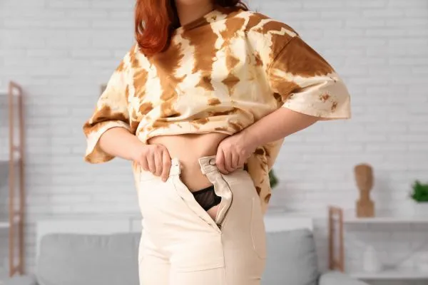 Image of woman trying to do her trousers up after pregnancy weight gain Chard